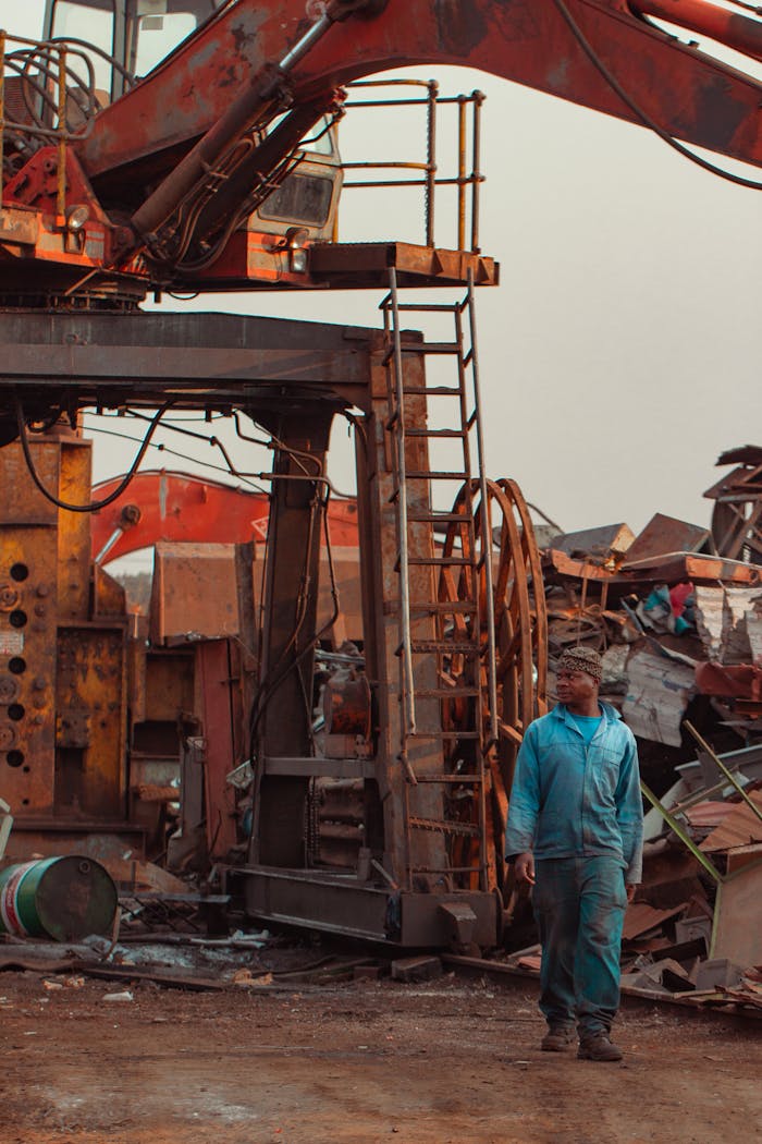 service-03 A construction worker stands in a busy scrap yard with heavy machinery around.