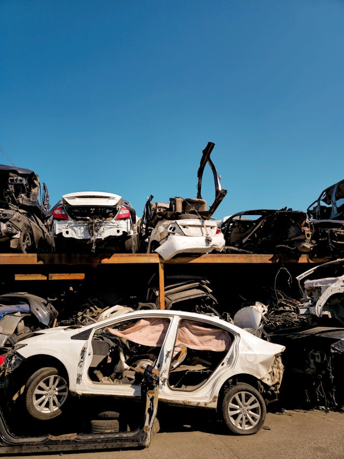 service-01 Rows of damaged vehicles in a scrapyard under a clear blue sky.